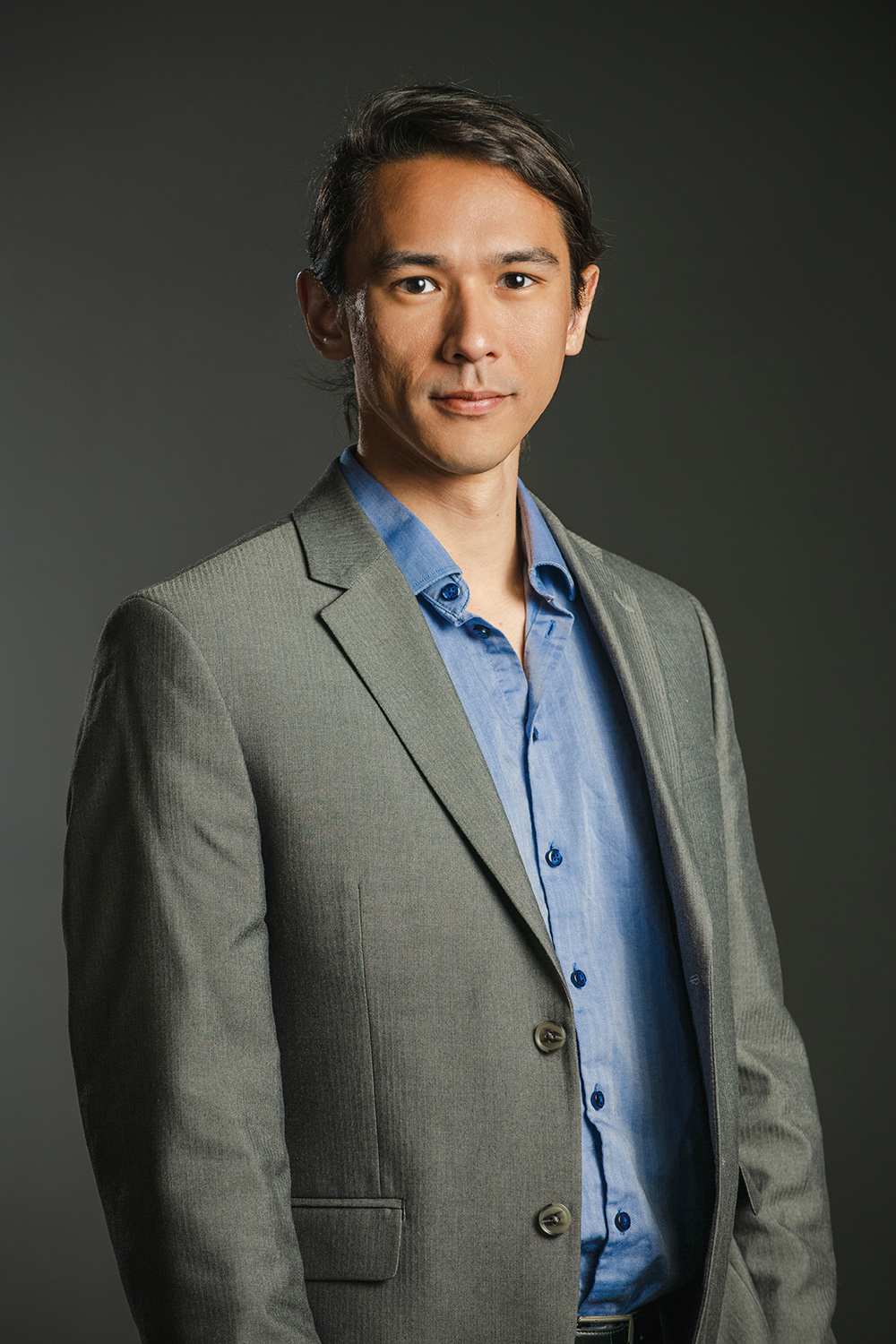Color photograph of an Asian man wearing a blue shirt and blazer looking at the camera