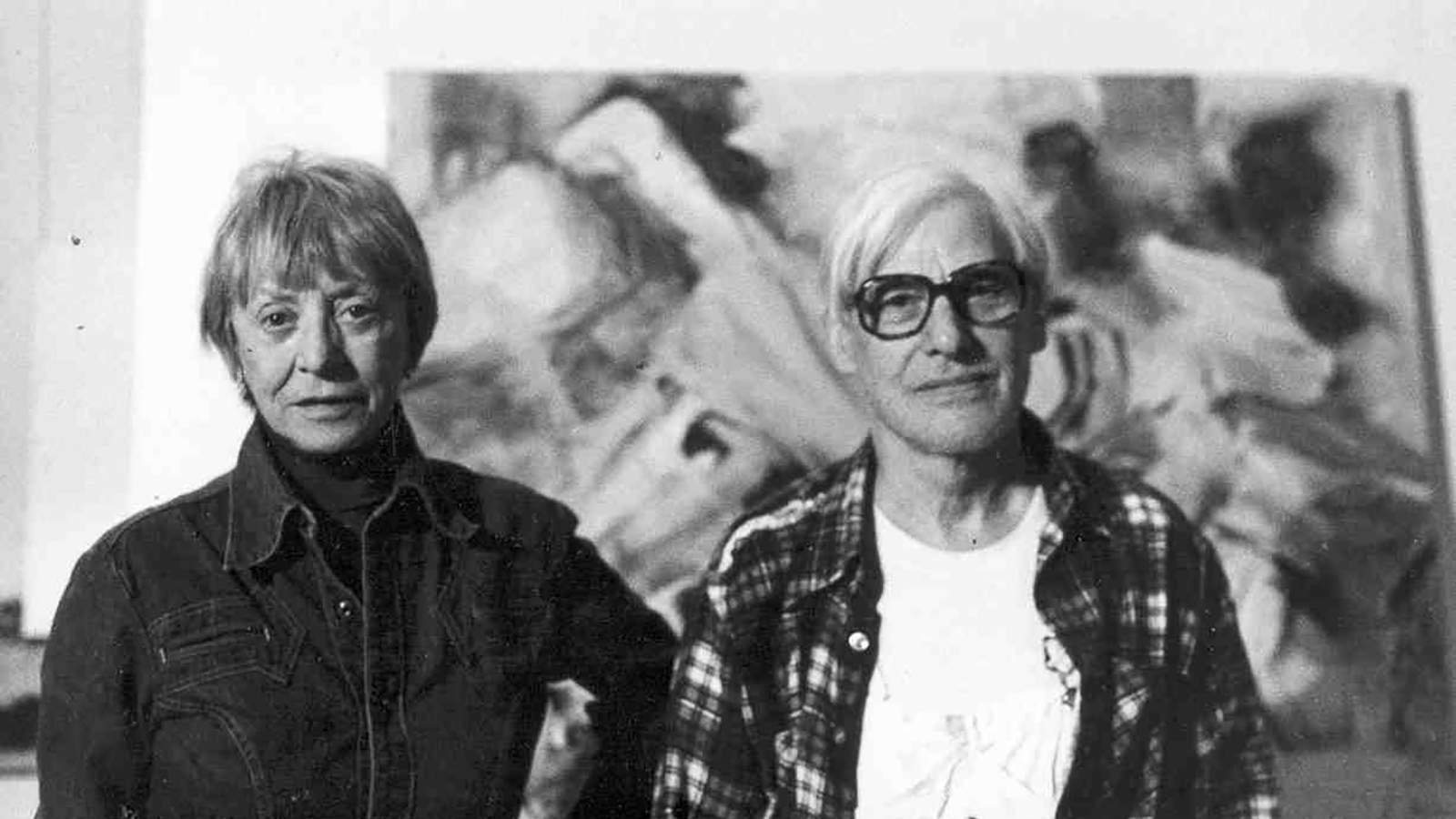 Black and white photograph of the heads and torso of Elaine and Willem de Kooning standing in front of an abstract painting