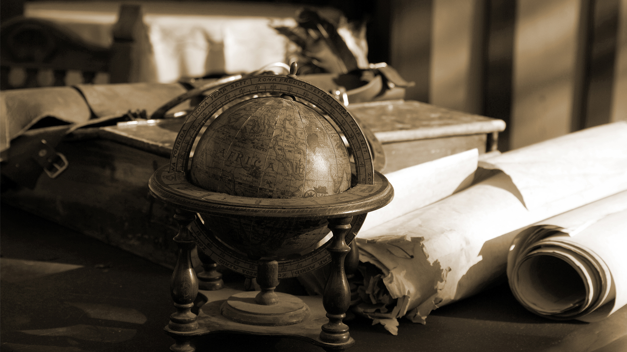 Color photo of a scholars desk with an old globe, scrolls, and other scholarly accoutrements
