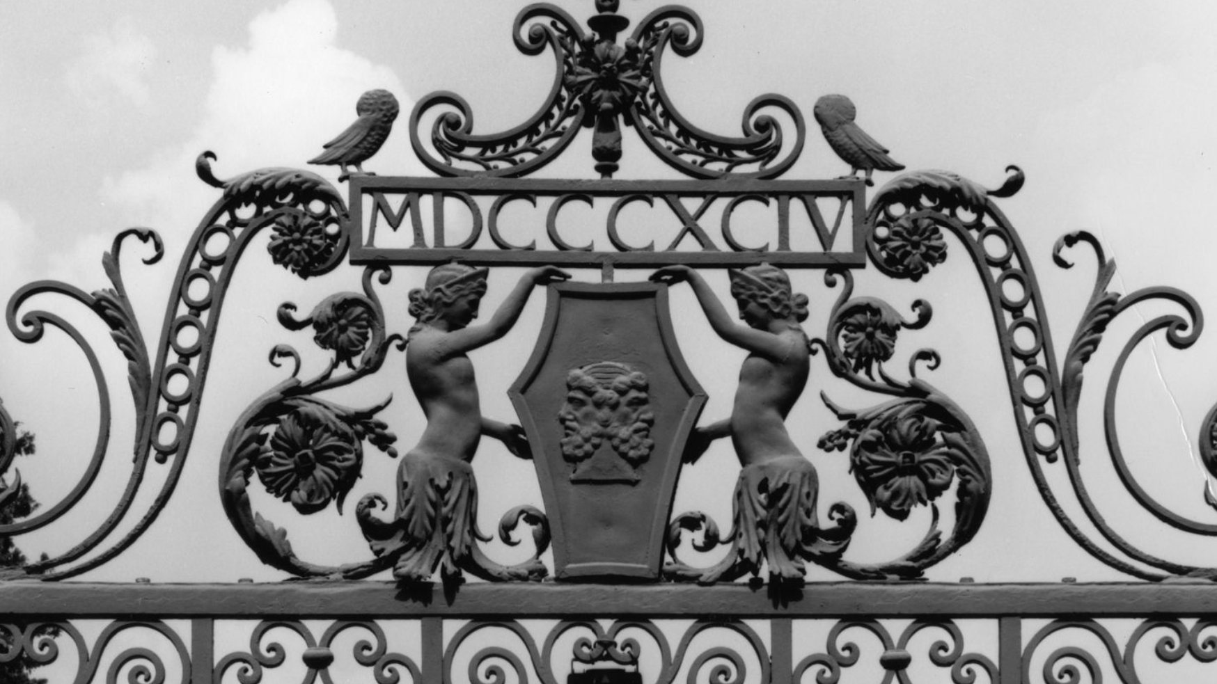 Black and white photo of figures and floral designs on the top of an iron gate