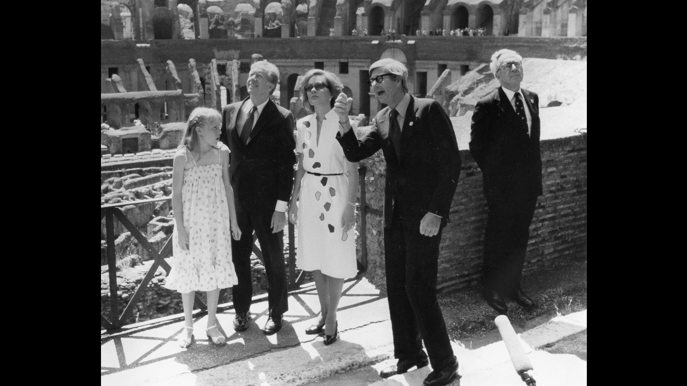 Black and white photograph of three men, one woman, and one girl on a tour in the Roman Colosseum