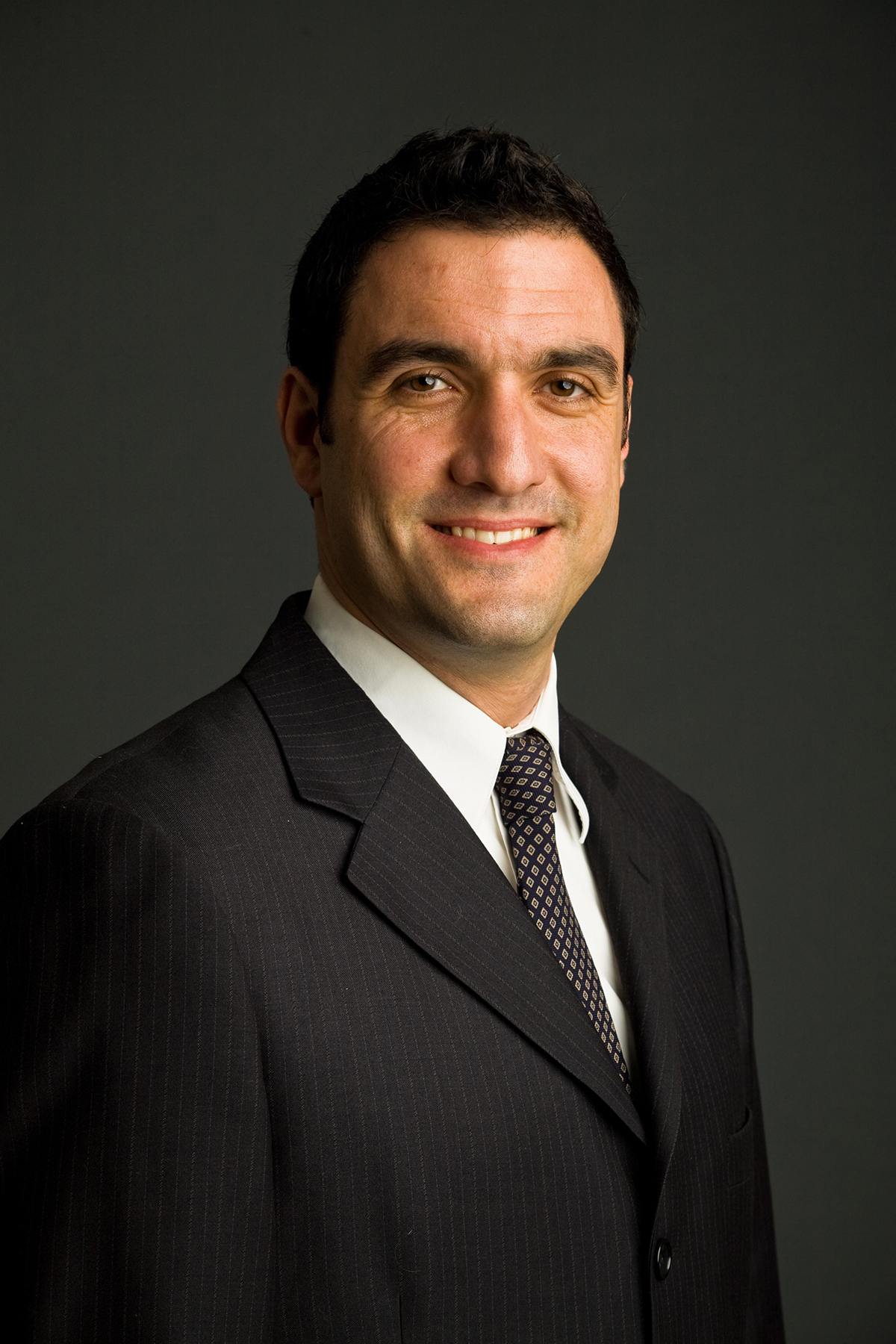 Andrew J. Kranis Color photograph of the head and torso of a light skinned man in a photographer's studio wearing a suit and tie and smiling at the camera