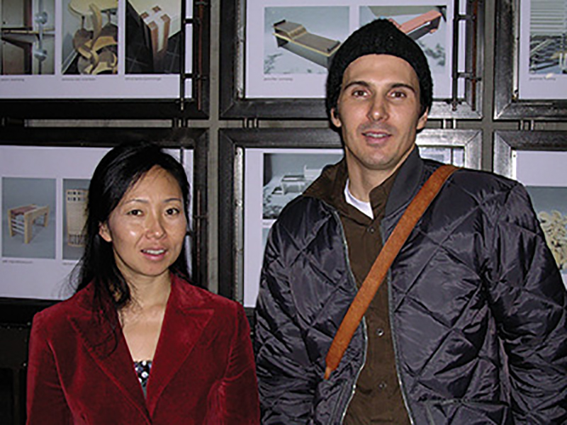 Annie Han and Daniel Mihalyo Color photograph of the torsos of an Asian woman wearing a red jacket and a light skinned man wearing a blue jacket, cap, and shoulder bag