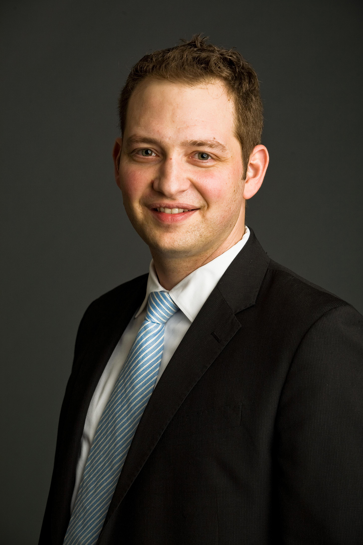 Christopher Counts Color photograph of the head and torso of a light skinned man in a photographer's studio wearing a suit and tie and smiling at the camera