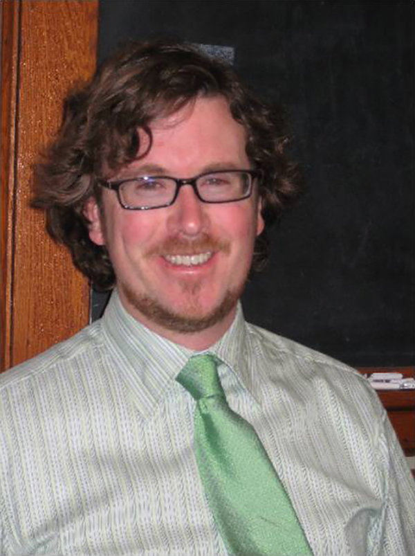 Christopher Macevitt Color photograph of the head and torso of a light skinned man wearing glasses and a shirt and green tie; he smiles at the camera