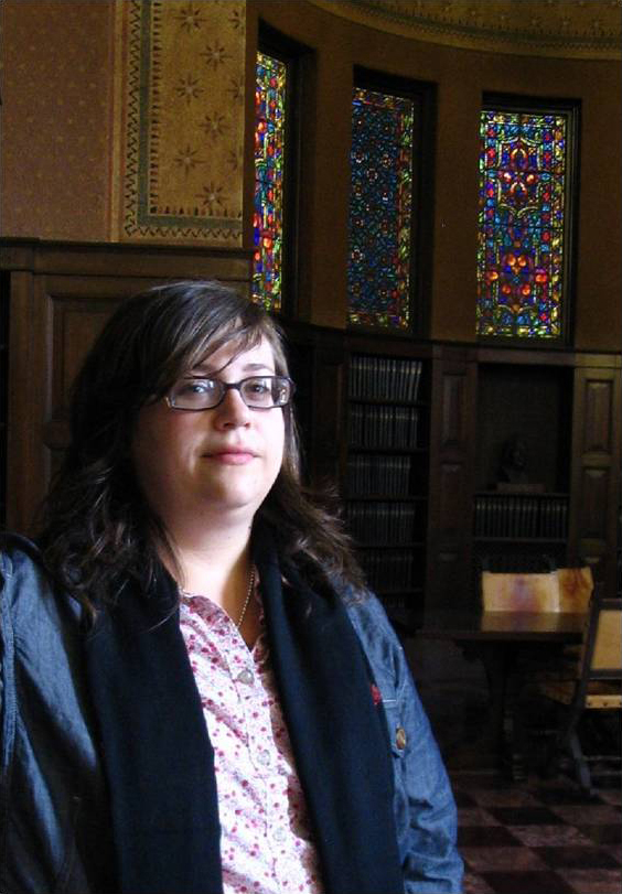 Eleanor M. Rust Color photograph of the head and torso of a light skinned woman wearing glass and standing in a dark wood-paneled room with stained glass windows
