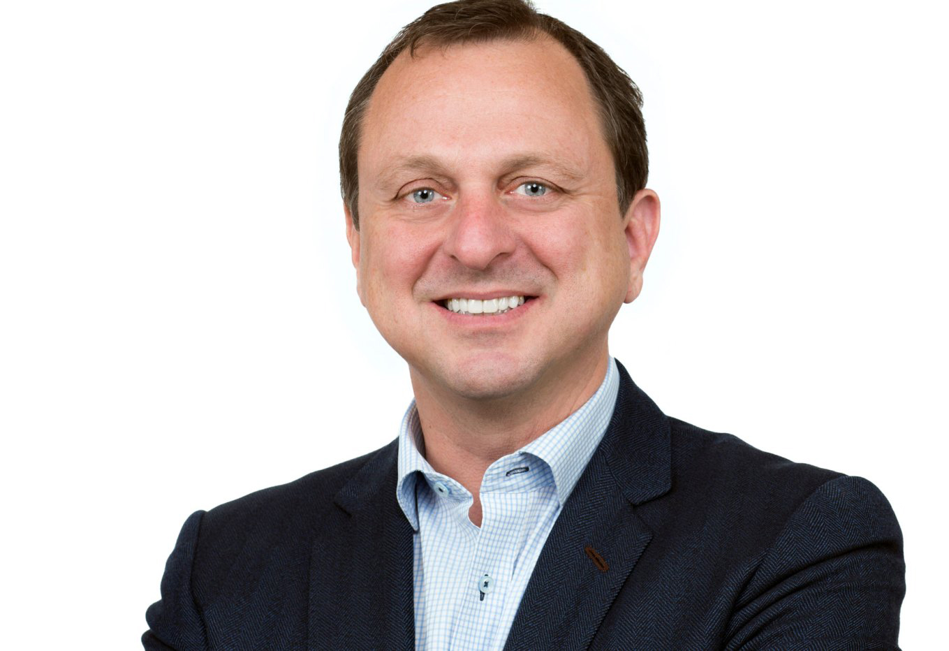 Gregg Pasquarelli Color photograph of the head and shoulders of a light skinned man smiling at the camera with a solid white background behind him