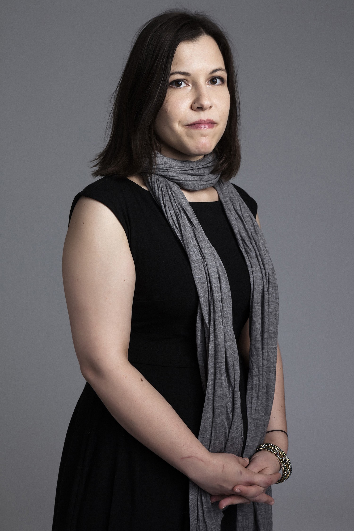 Irene SanPietro Color photograph of a light skinned woman from the waist up; she wears a dark sleeveless dress and a scarf around her neck that falls down in front of her