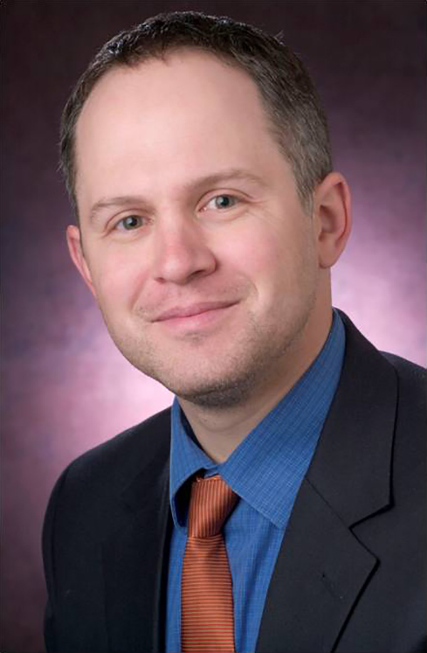 Kevin Uhalde Color photograph of the head and chest of a light skinned man wearing a suit and tie and smiling at the camera