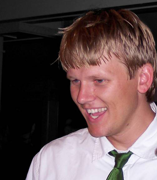 Kiel Moe Color photo of the head and shoulder of a light skinned man with blond hair wearing a white shirt and green tie