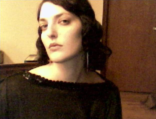 Lisa Tziona Switkin Color photograph of the head and shoulders of a light skinned woman with dark hair and a dark top vamping for the camera