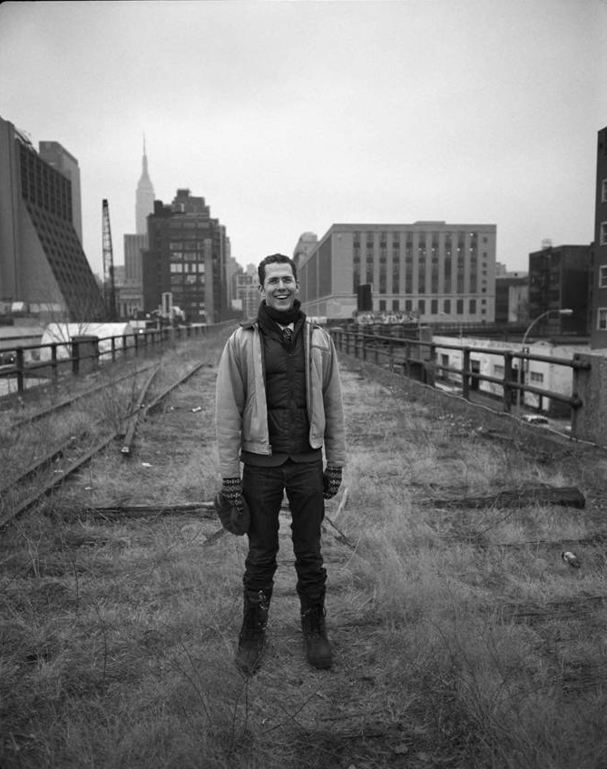 Robert Hammond Black and white photograph of a light skinned man dressed with a scarf, jacket, and gloves and standing on an abandoned elevated railroad track