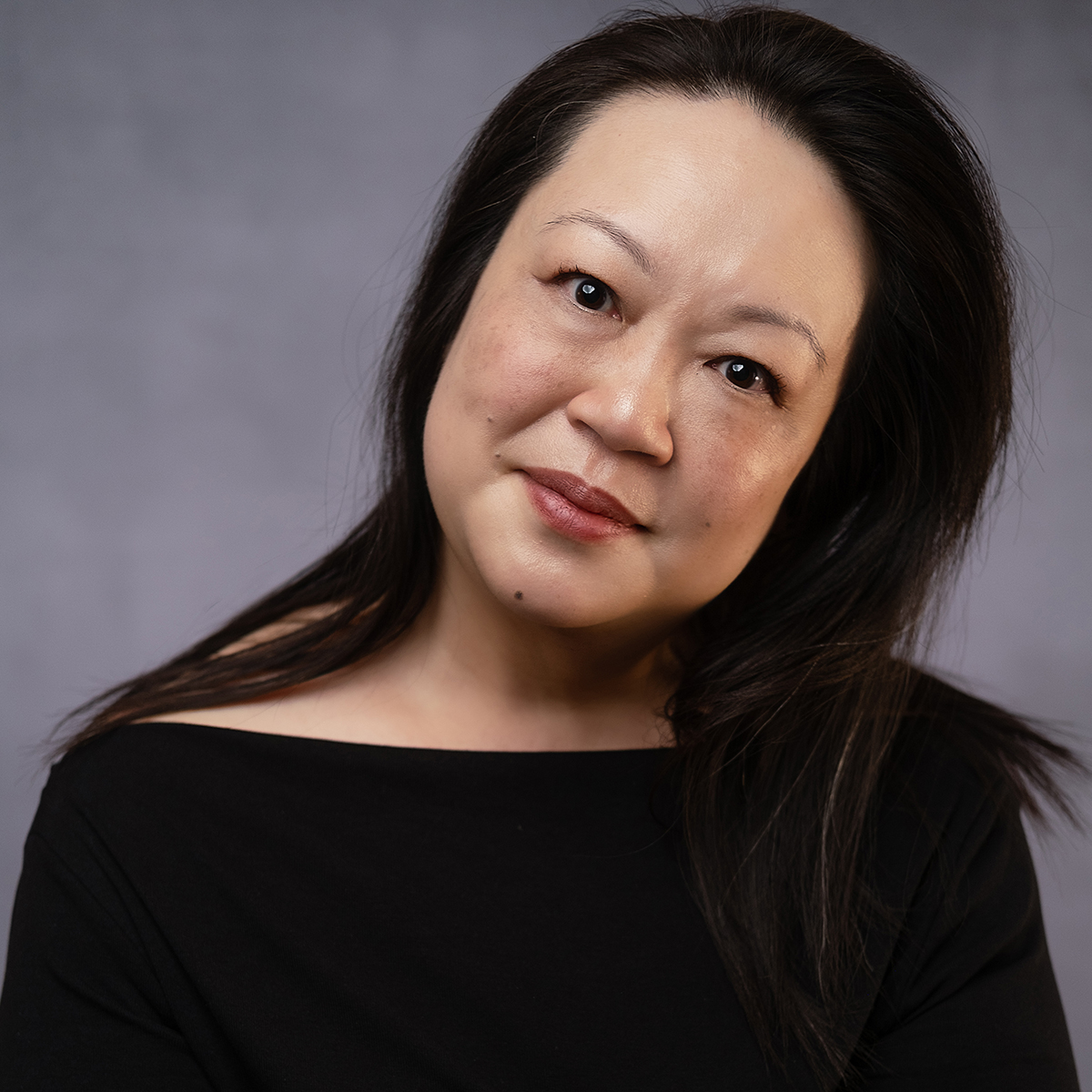 Staff - Aliza Wong A color photograph of the head and torso of an Asian woman; she tilts her head to the left while looking directly at the camera