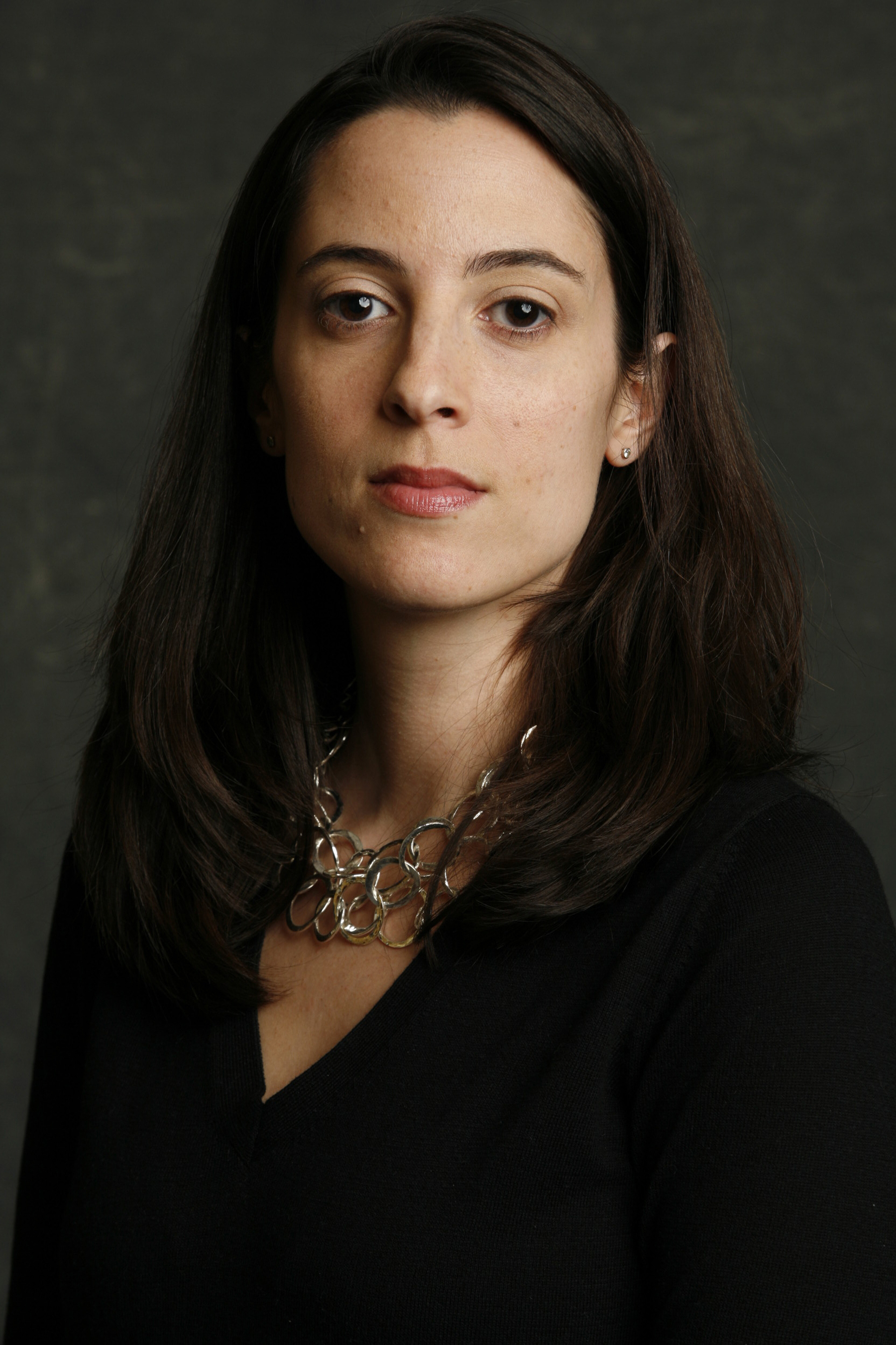Susanna McFadden Color photo of the head and torso of a light skinned woman with dark hair in a photographer's studio, looking at the camera with a serious expression