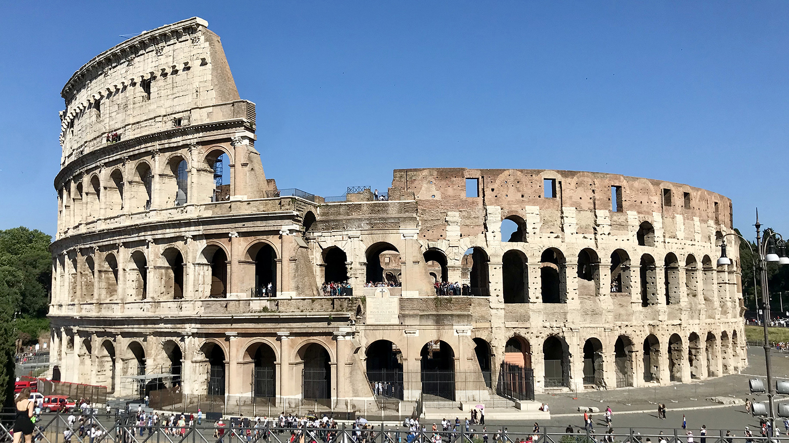 Color photograph of the full Roman Colosseum on a sunny, cloudless day with blue skies