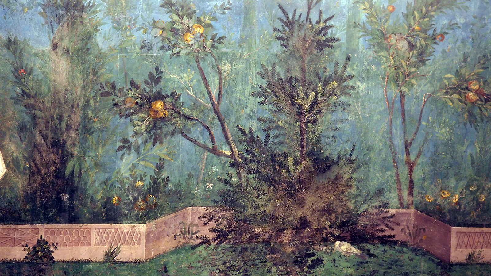 Color photograph of an ancient roman wall mural depicting fruit-bearing plants and trees and a small fence running along the bottom