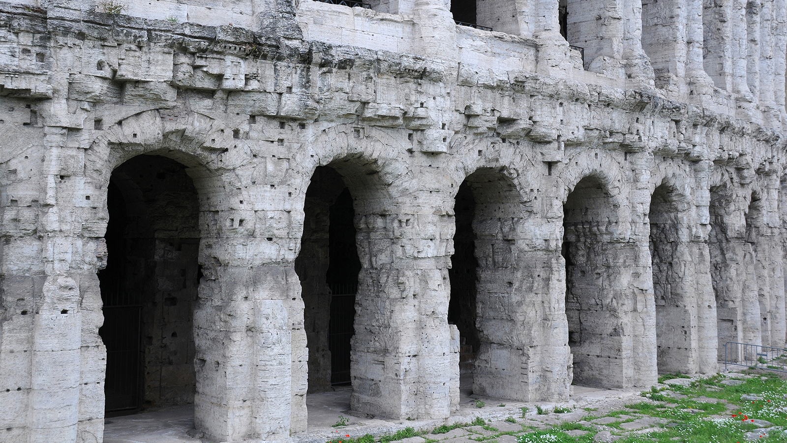 Color photograph of the ground level of the exterior of ancient roman theater, showing a half dozen arched entryways