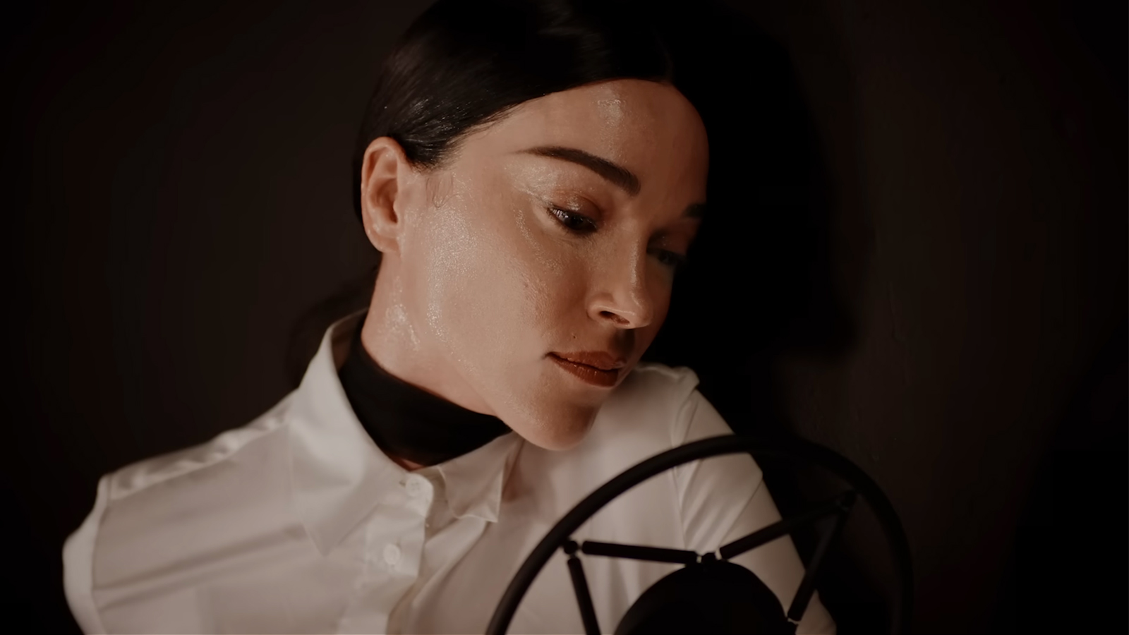 Still from a color video showing the side of a white woman's face looking down at a microphone