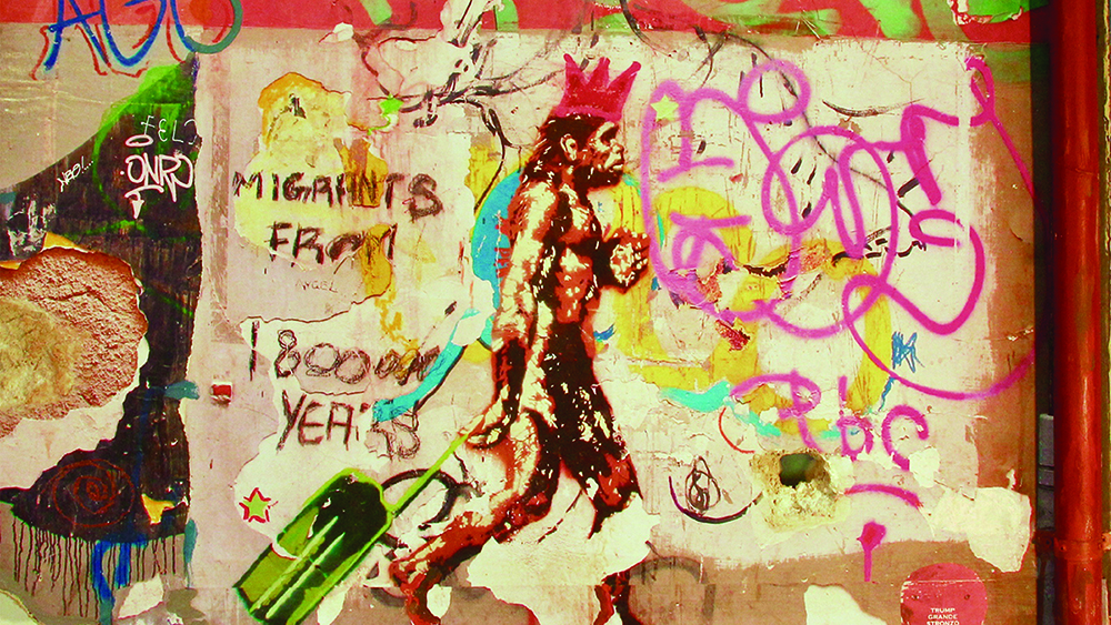 Detail of a book cover showing a Franc Palaia painting depicting the profile of a neanderthal-like man walking and pulling a luggage on wheels; the background depicts a multicolored graffitied wall