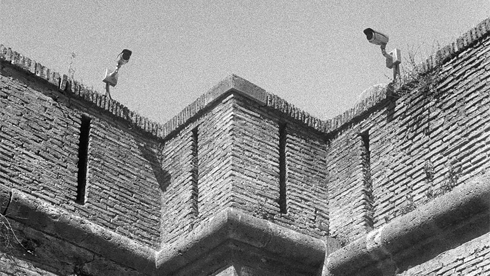 Black and white photograph of Vatican City walls, with two security camera mounted on the top