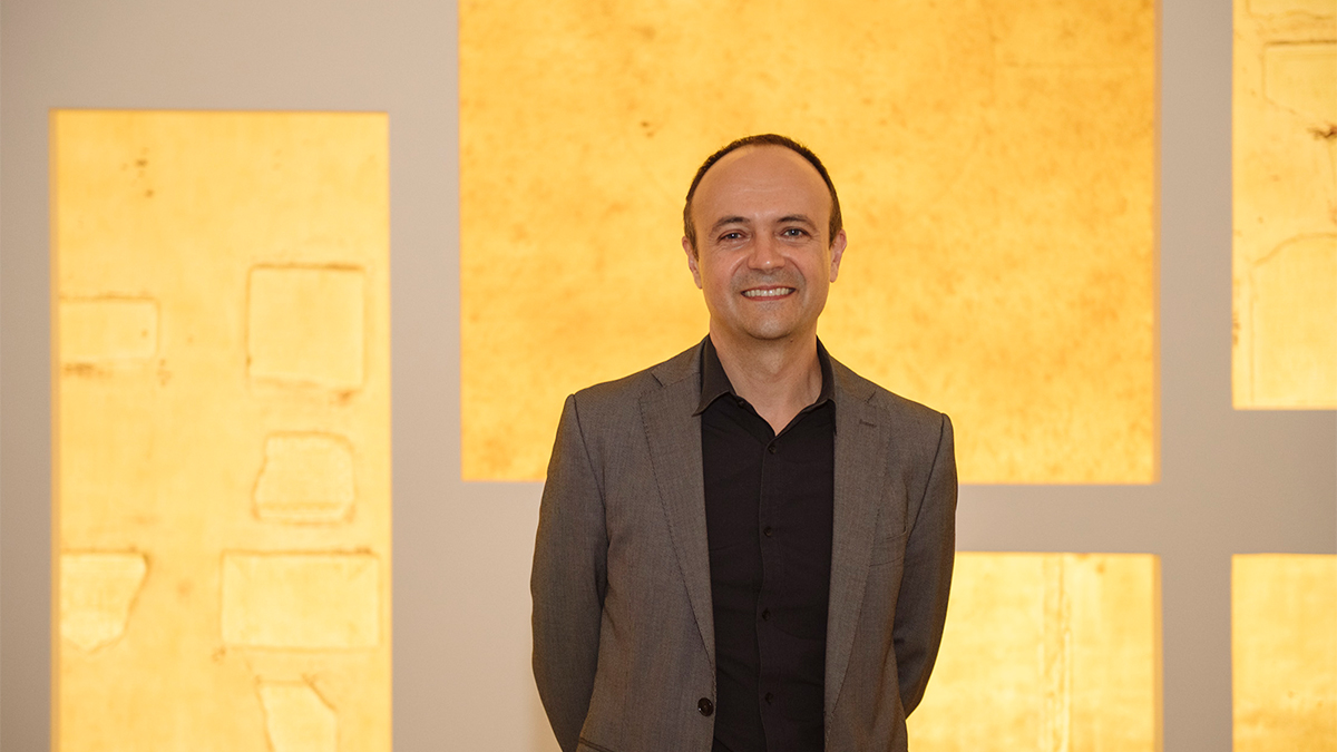Color photo of a light skinned man smiling at the camera and standing in front of his latex wall art