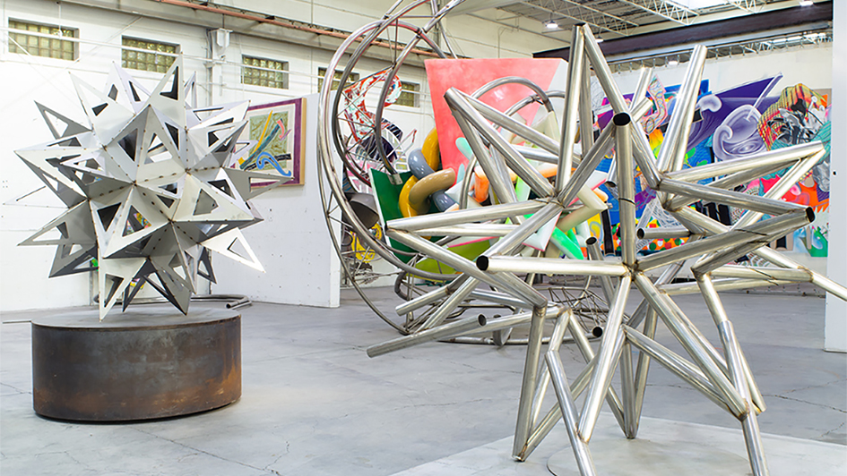 Color photo of an artist studio with two large metal sculptures shaped like many pointed stars