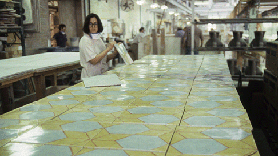Color photograph of a table with artist's prints, with a woman artist in the background inspecting them