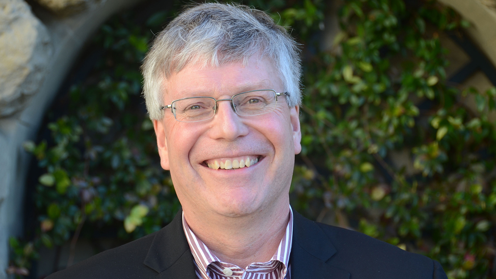 Color photo of the face of a light skinned man with silver hair smiling at the camera