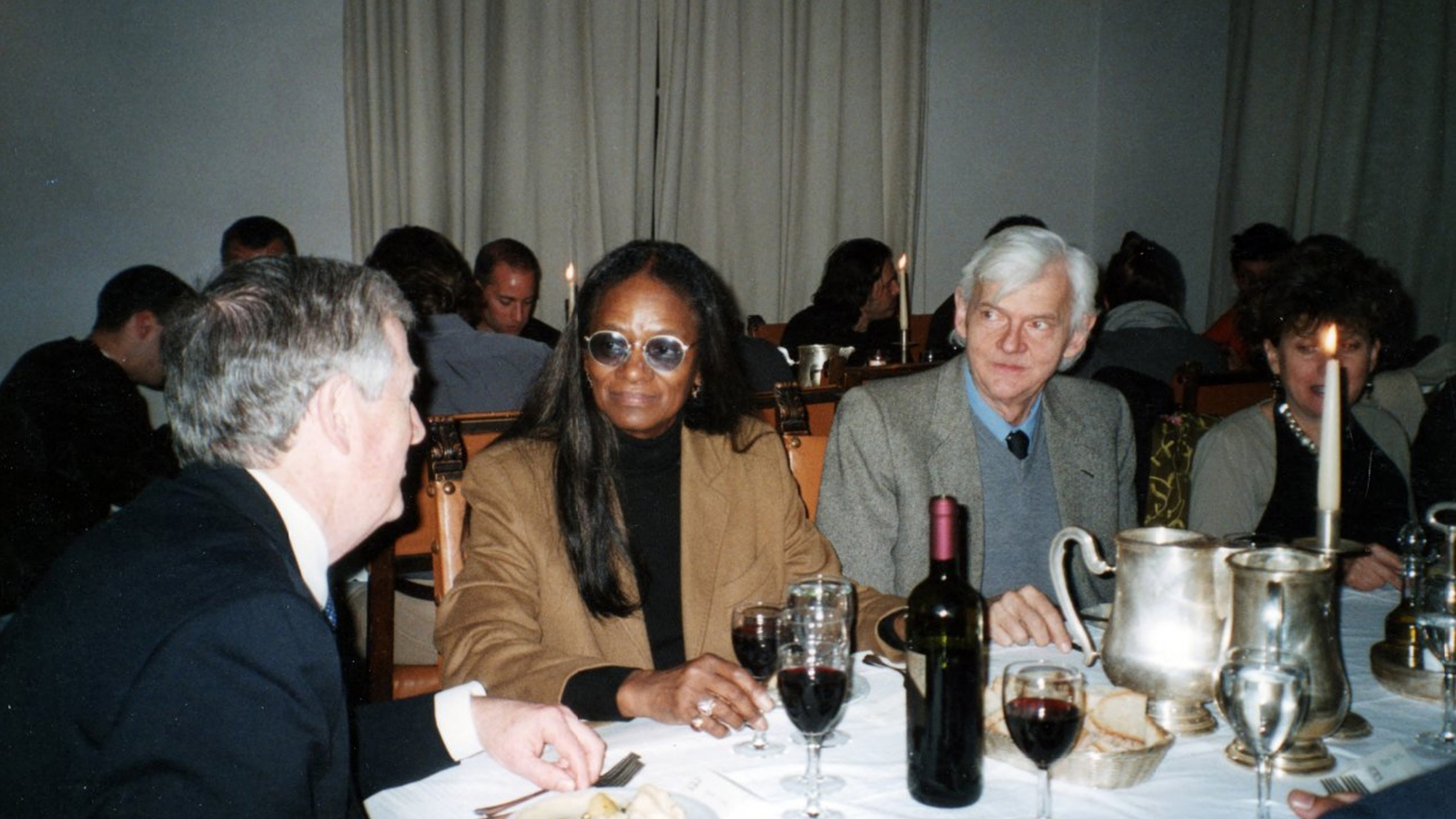 Color photograph of a dinner table with Barbara Chase Riboud flanked by two white men
