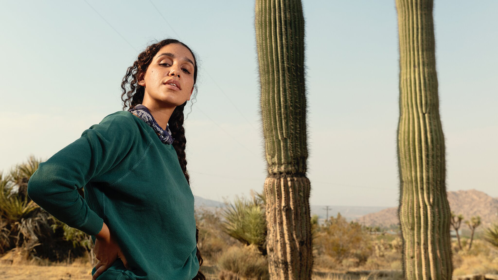 Color photograph by Djeneba Aduayom of Garrett Bradley standing next to two cacti in a California desert environment