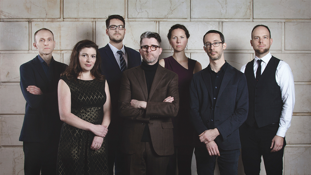 Color photo of seven people standing in front of a block wall