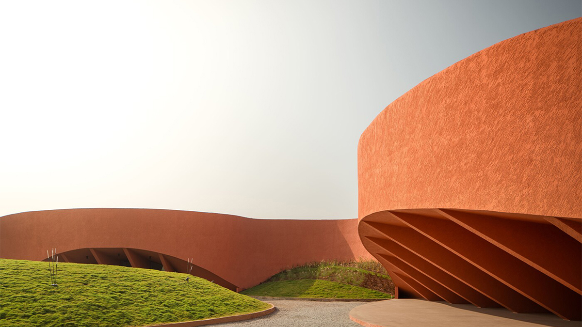 Color photo of a rust colored curved modern building and a cloudy sky