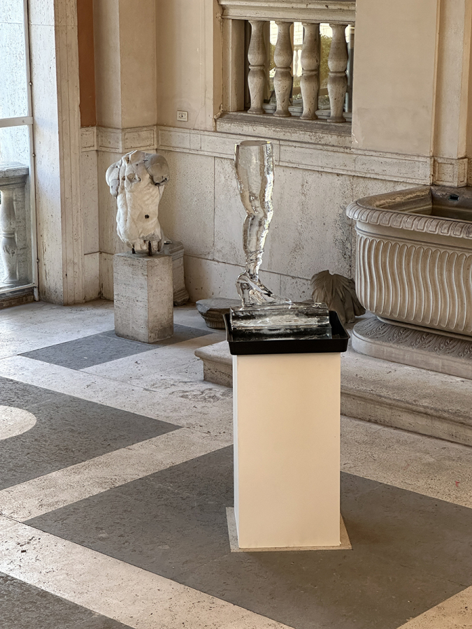 color photo of a melting ice sculpture of a human leg and shoe in a roman patio