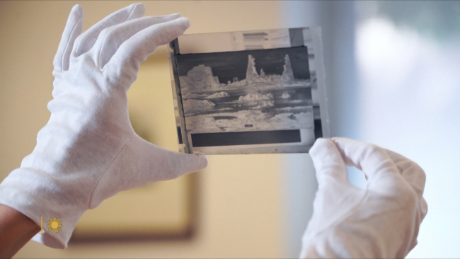 A pair of gloved hands hold up a black and white photographic negative