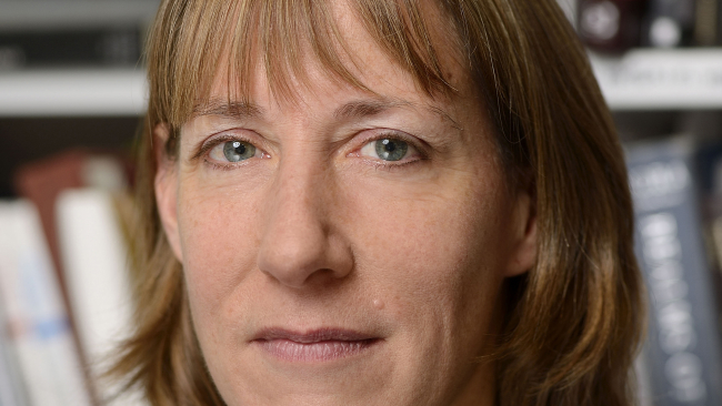 Color portrait of the face of Elizabeth Rodini standing in front of her bookshelves