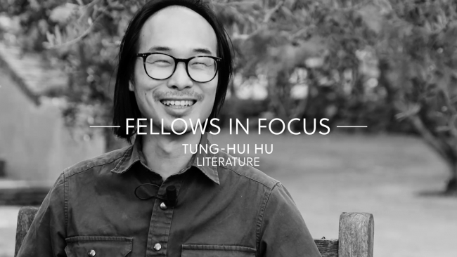 Black and white video still depicting an Asian man wearing glasses and smiling off camera; overlaid on the image are white letters that read Fellows in Focus, Tung-Hui Hu, Literature