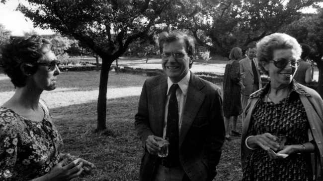 Black and white photograph from 1978 depicting two light skinned women flanking a light skinned man; they stand in a Roman garden