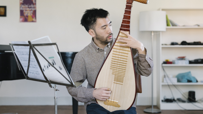 A young man plays on a pipa (musical instrument), a music stand to his right