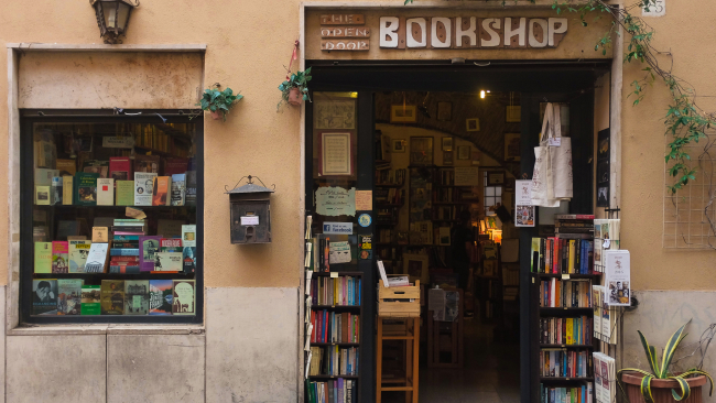 Color photograph of the exterior of a bookshop in Rome, books on shelves as seen through an open door and closed window