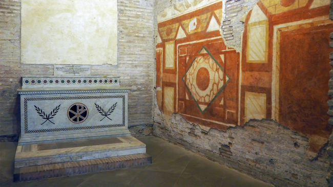 Color photograph of an ancient Roman house with a geometric wall mural painted with browns and yellows